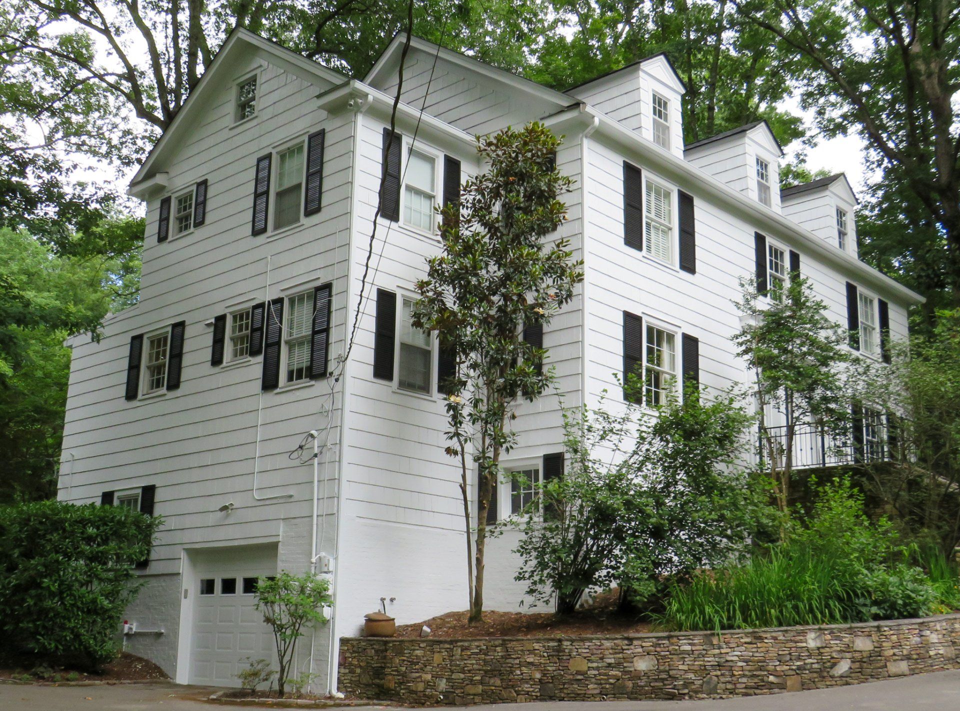 A large white house with black shutters is surrounded by trees