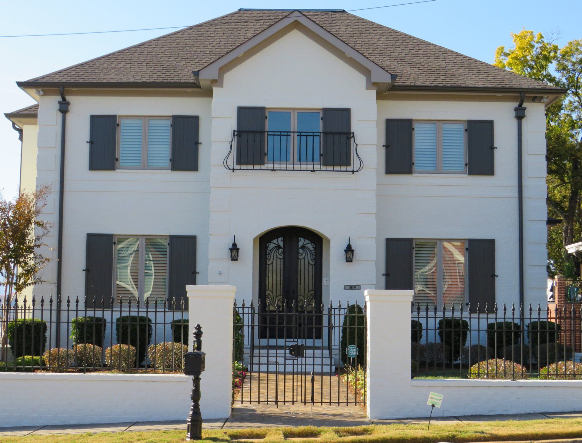 A white house with black shutters and a wrought iron fence