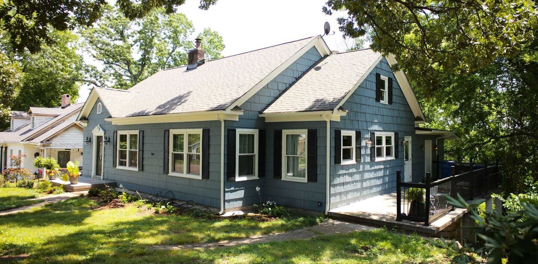 A blue house with white shutters is surrounded by trees