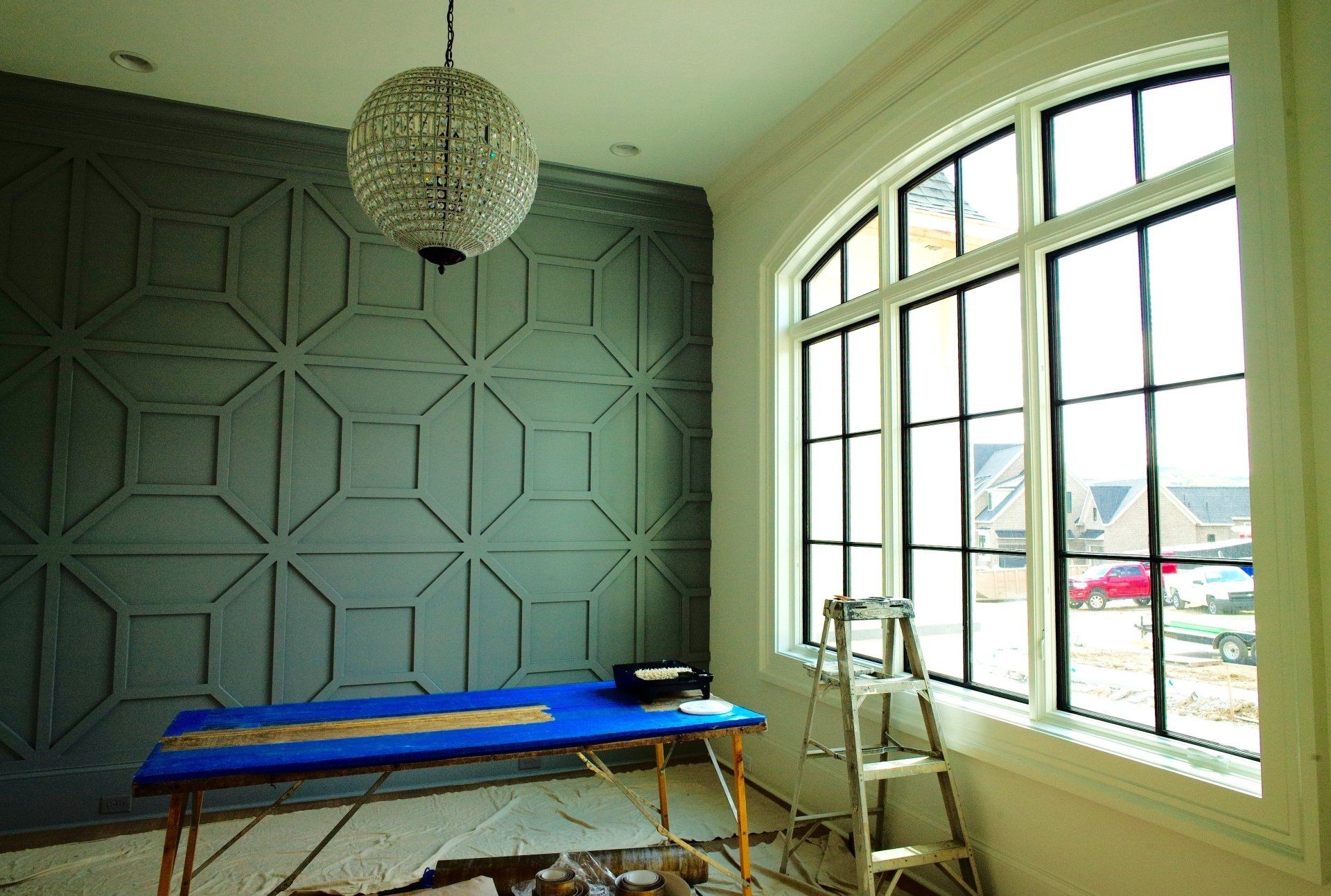 A room with a blue table and a ladder in front of a large window.