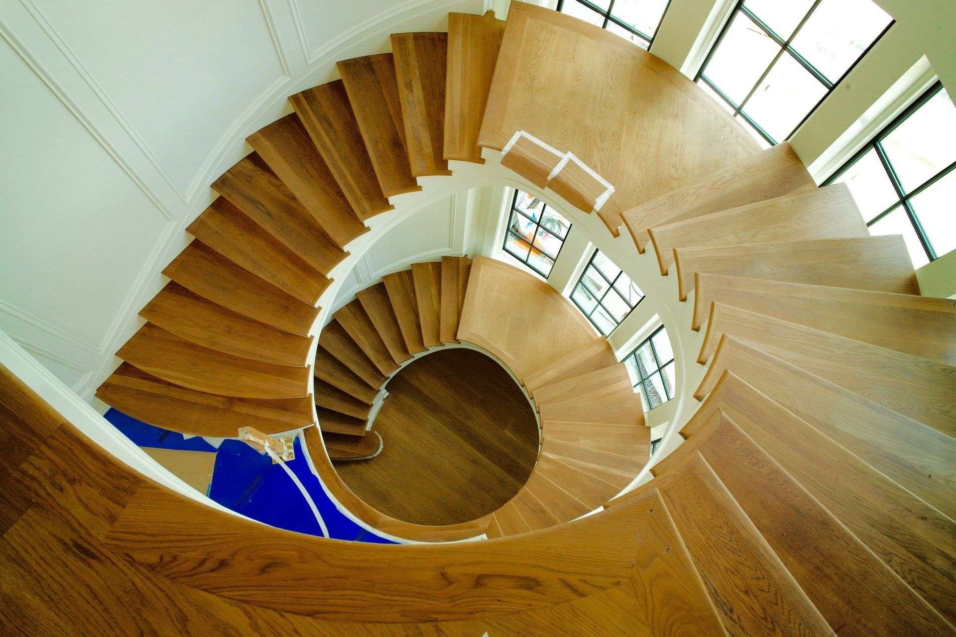 A wooden spiral staircase in a house with lots of windows