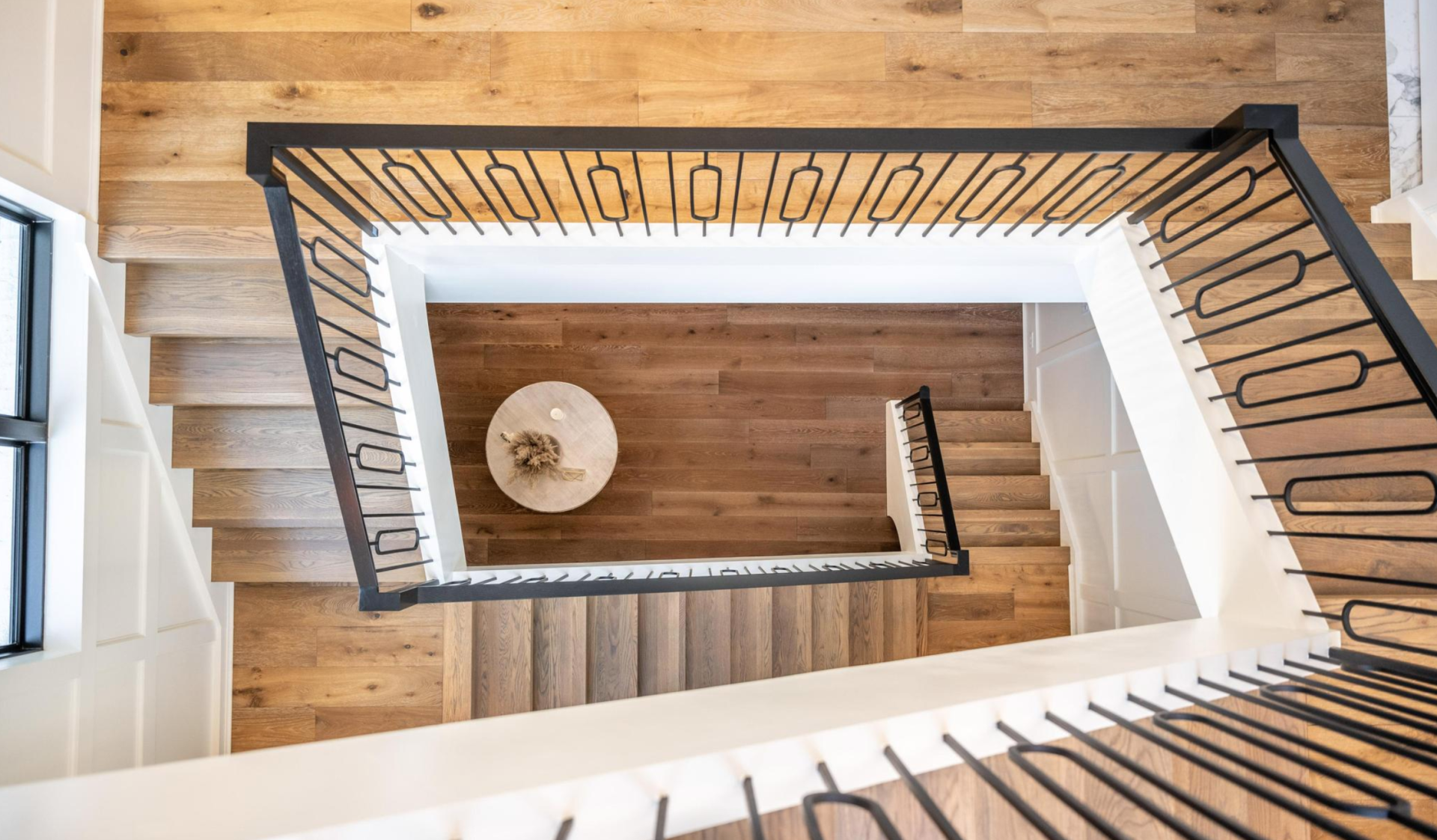 An aerial view of a spiral staircase with wooden steps and a black railing.