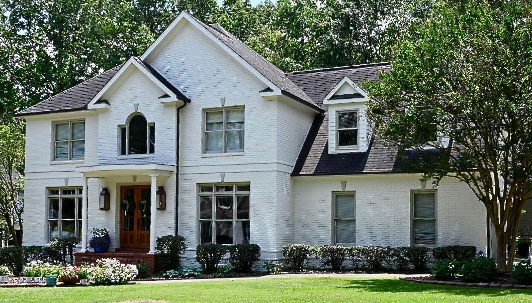 A large white house with a black roof is surrounded by trees.