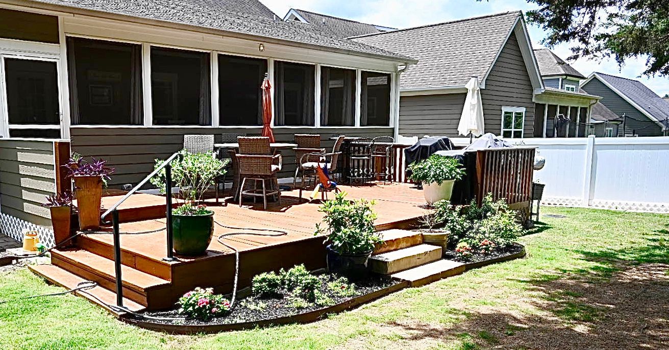 A screened in porch with a wooden deck and chairs in front of a house.