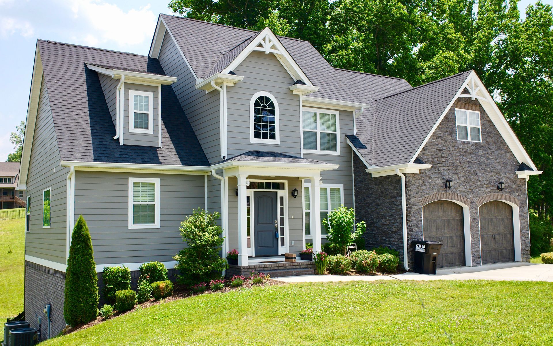 A large gray house with a black roof is sitting on top of a lush green hillside.