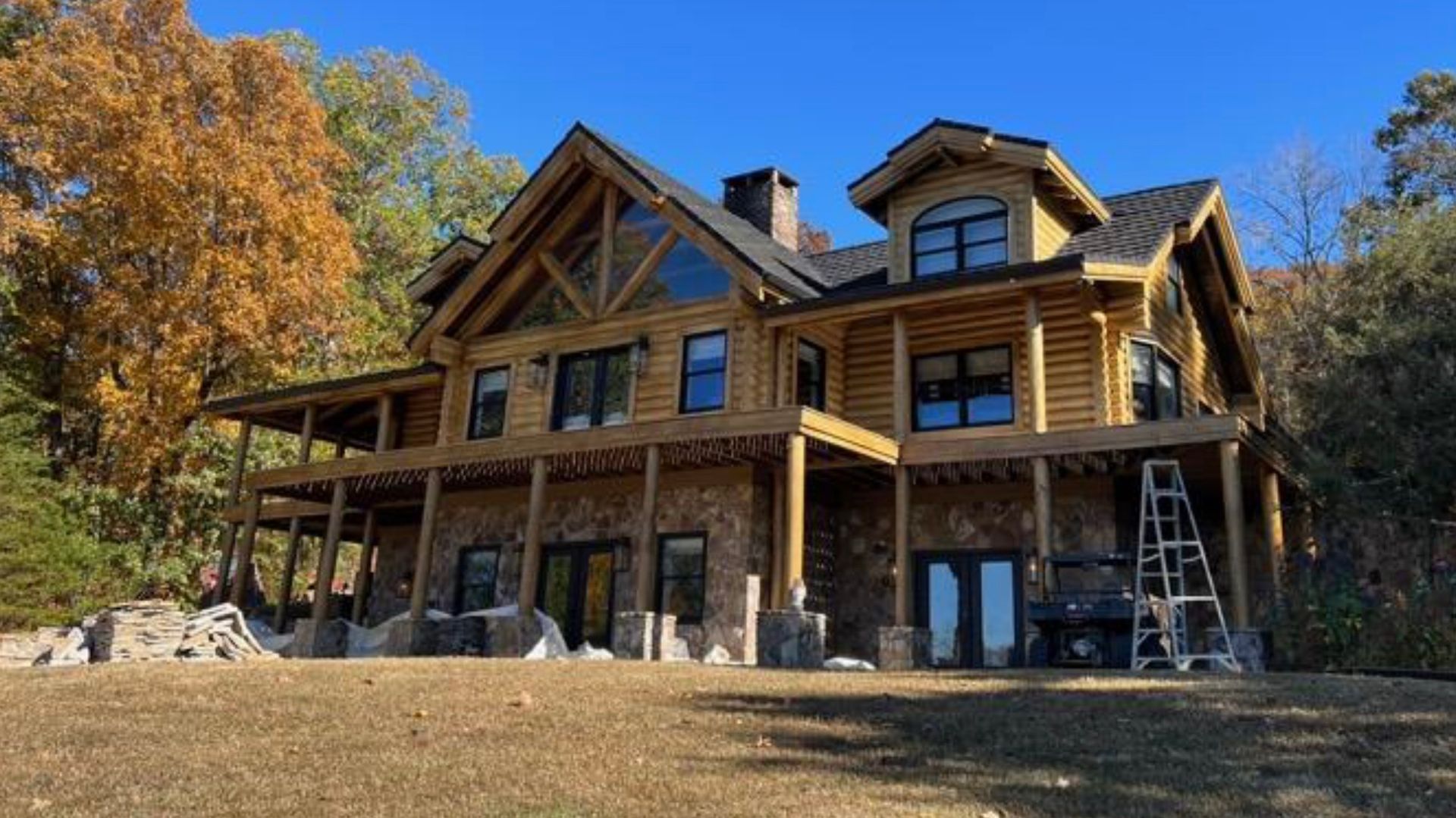 A large log cabin is sitting on top of a hill in the middle of a forest.