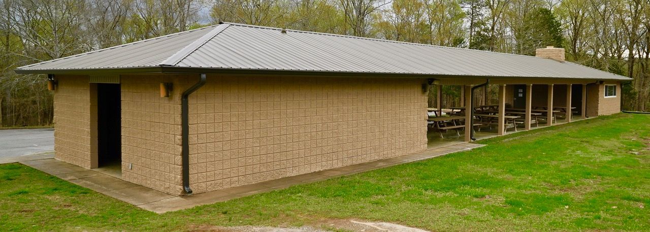 A large brick building with a metal roof is sitting on top of a lush green field.
