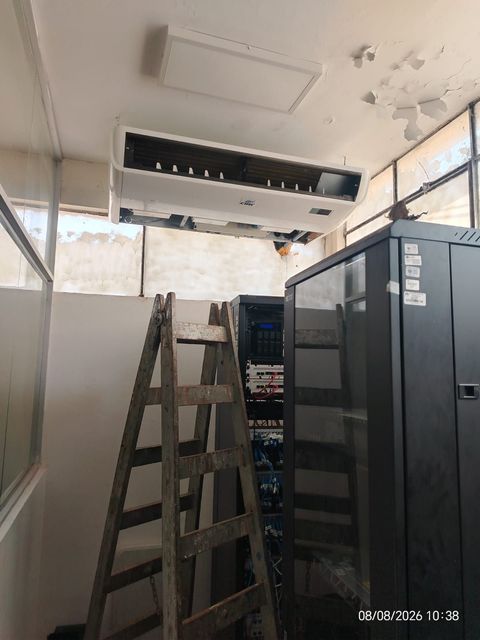 Escalera en una habitación estrecha junto a armarios de servidores, con un aire acondicionado montado en la pared encima.