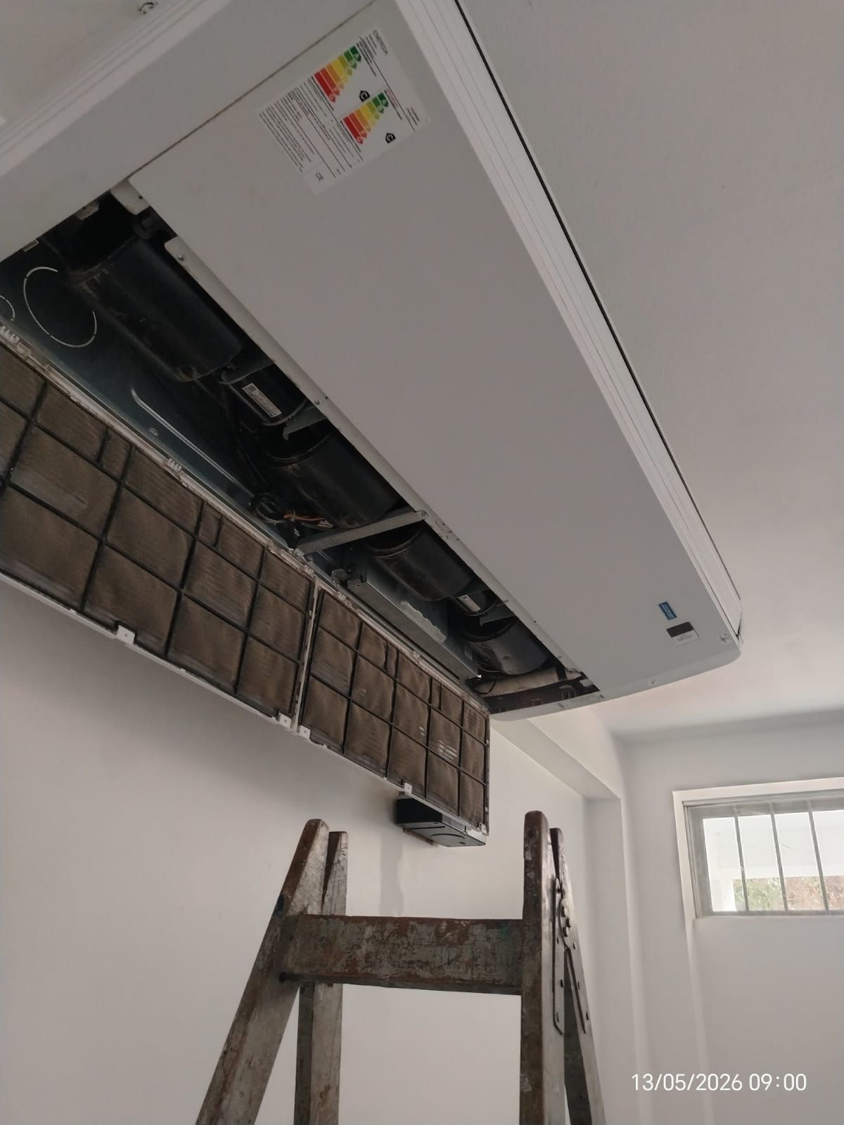 Se está instalando un aire acondicionado blanco de pared en el interior de una vivienda, subido a una escalera.