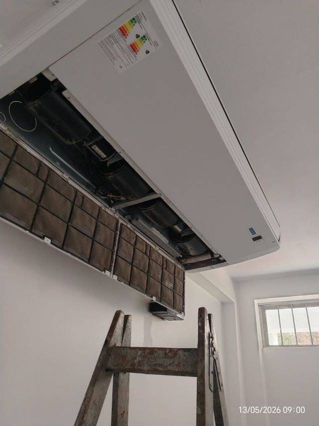 Se está instalando un aire acondicionado blanco de pared en el interior de una vivienda, subido a una escalera.