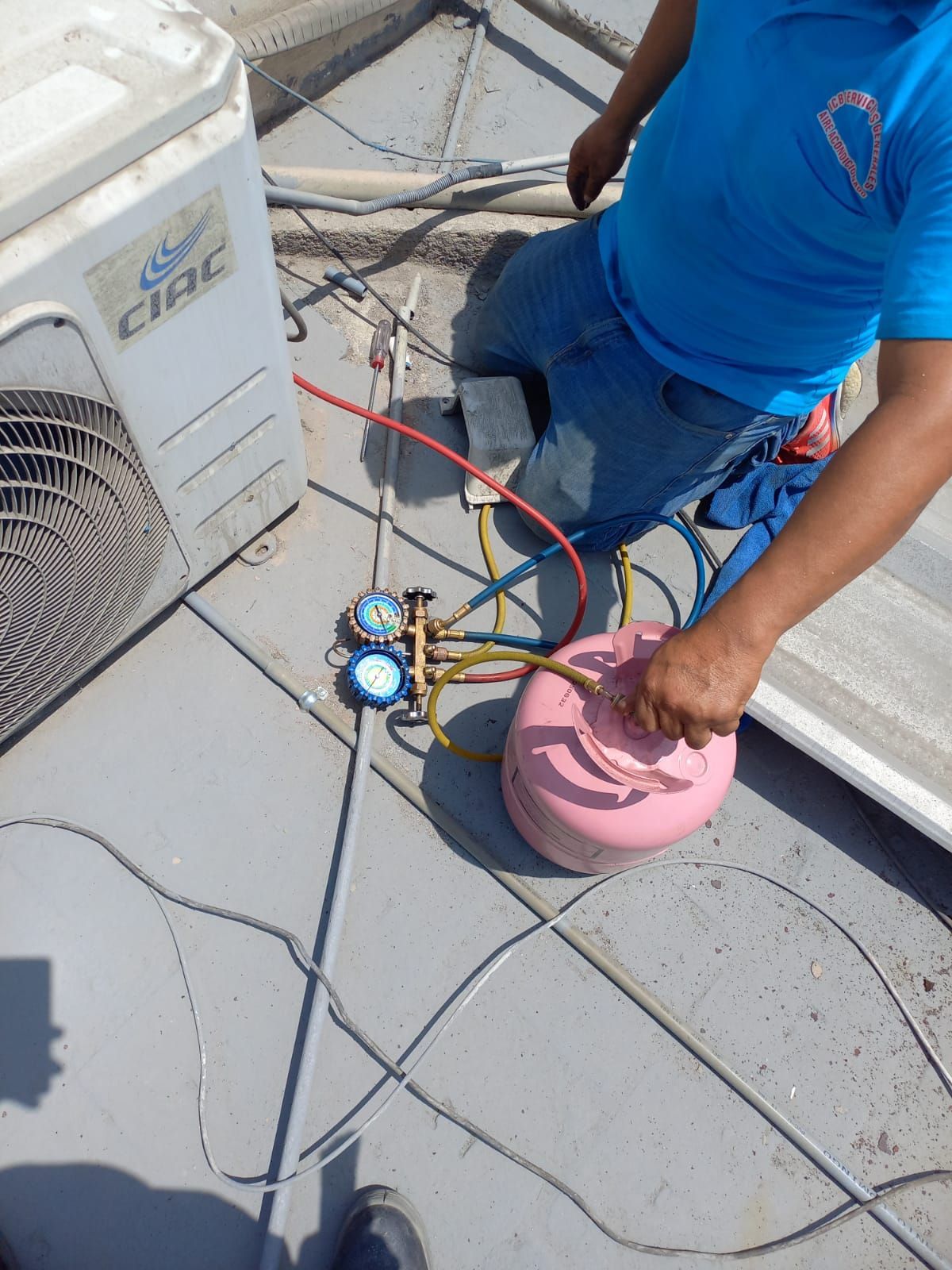 Técnico realizando el mantenimiento de una unidad de aire acondicionado exterior con manómetros y mangueras en una azotea.