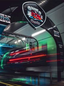 Car in motion going through a car wash, with neon lights and a business sign.