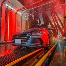 Car in a car wash, illuminated with red lights, being sprayed with water.