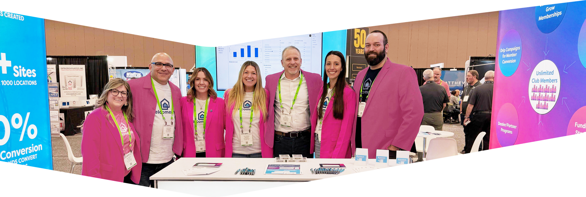 A group of people wearing pink jackets pose at a conference booth.