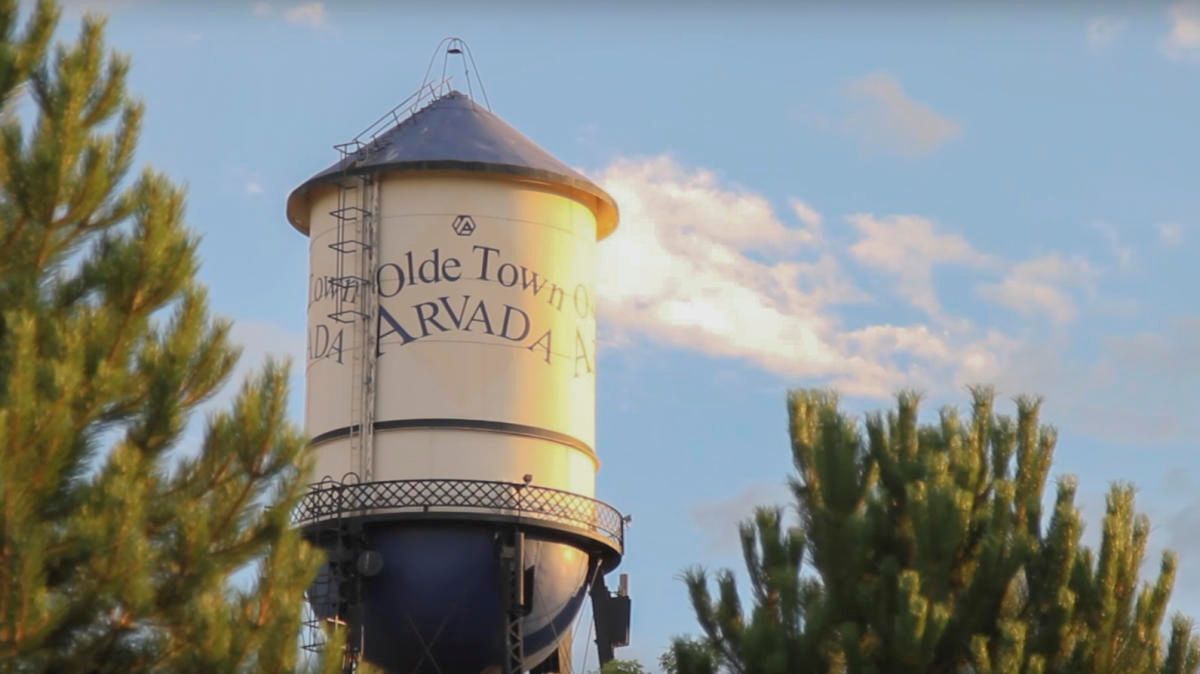Water tower with “Olde Town” and “Paradise” text, framed by pine trees at sunset.