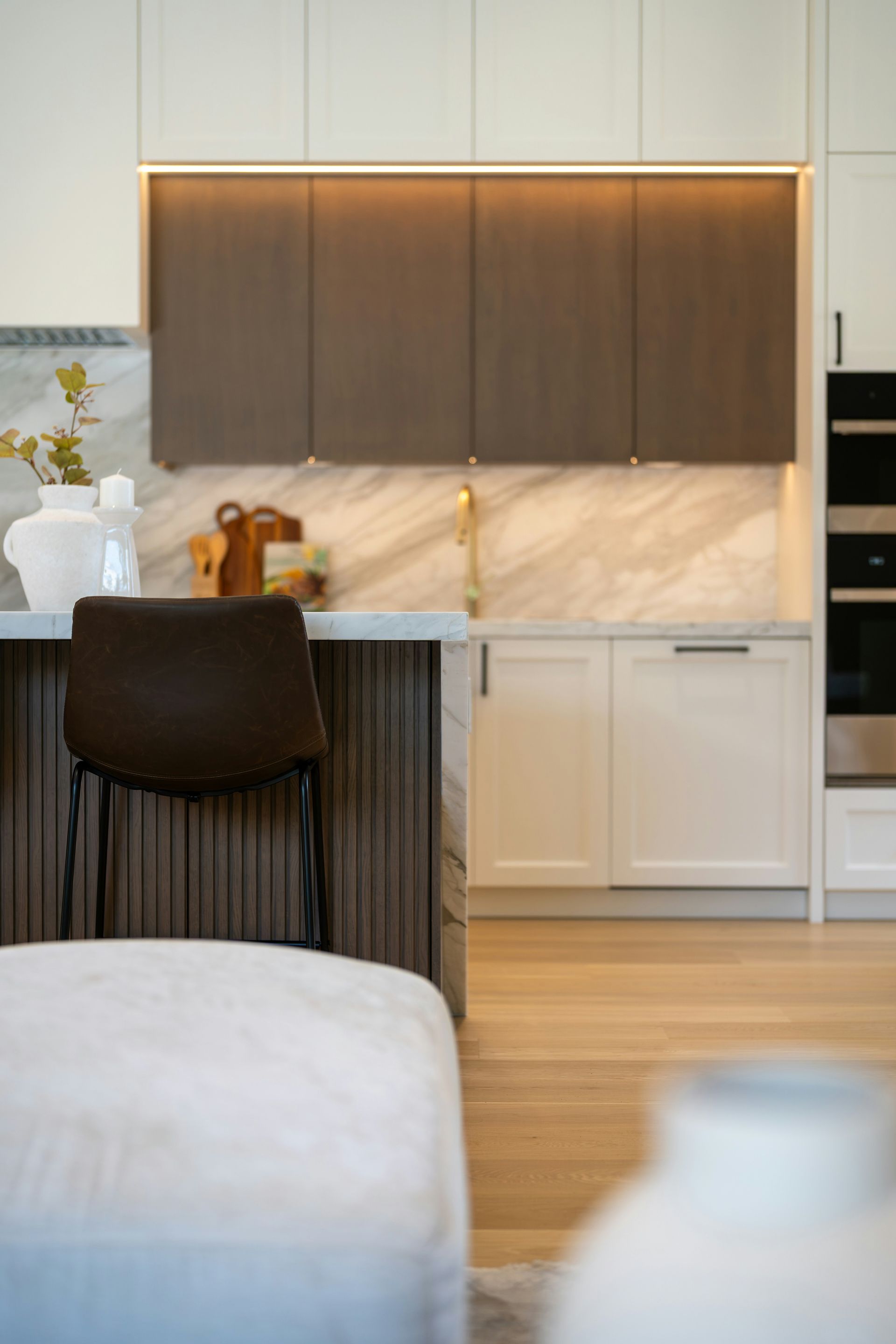 Modern kitchen with dark wood cabinets, marble backsplash, and a barstool by a white island countertop