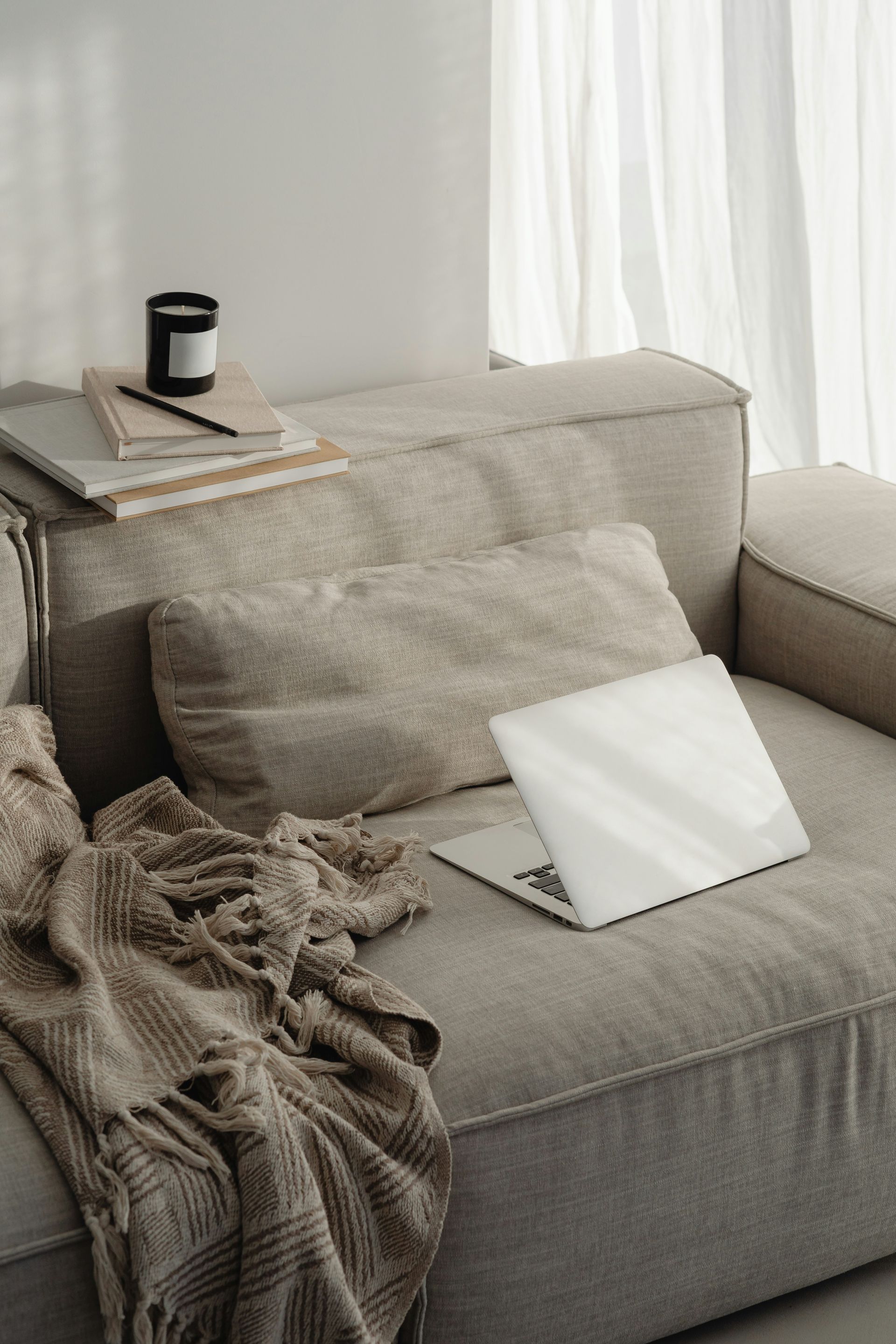 Cozy gray armchair by a window with blanket, pillow, and open laptop on the seat.