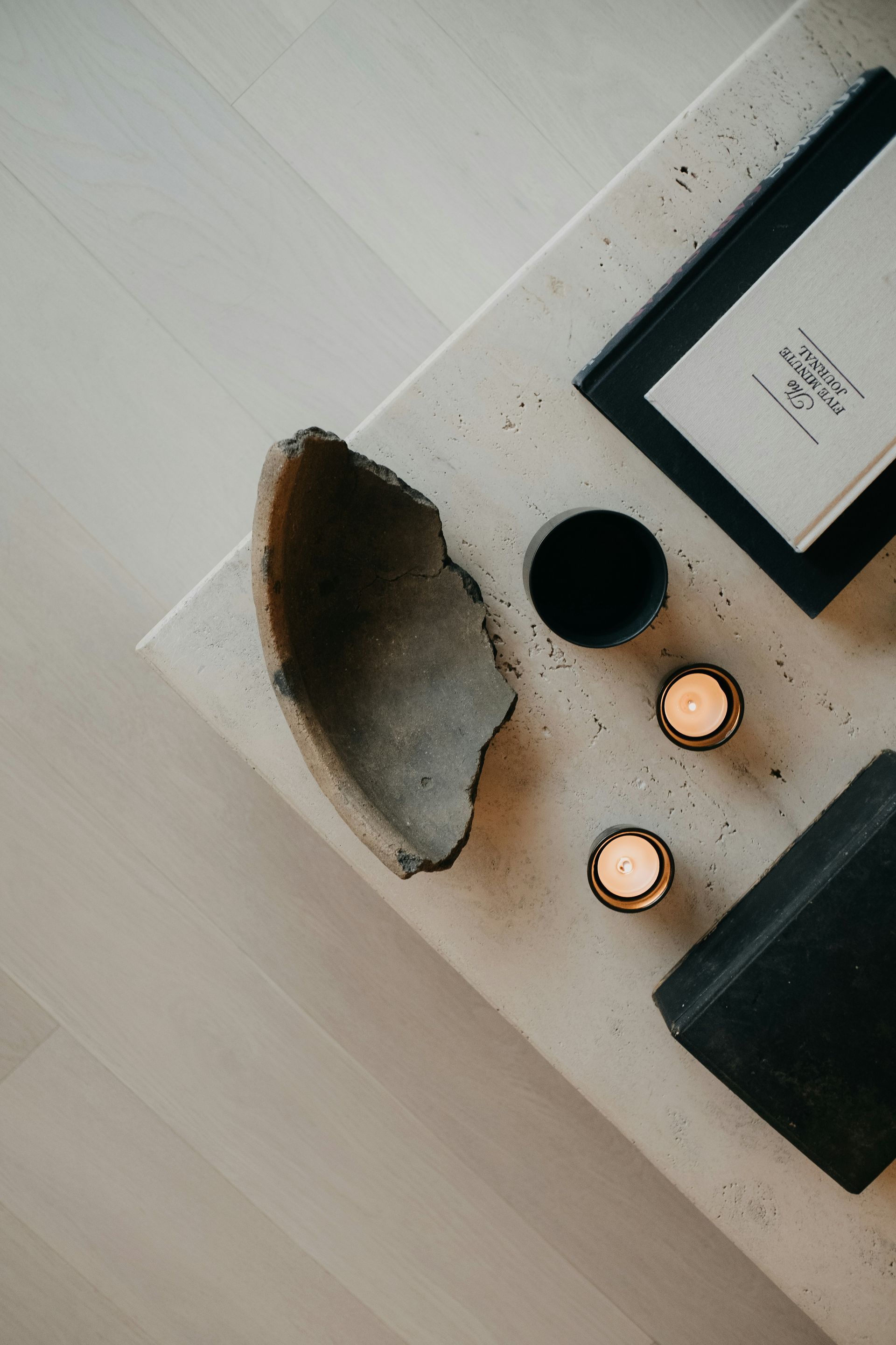 Cozy tabletop with candles, a framed print, a black cup, and a decorative bowl on a light surface.