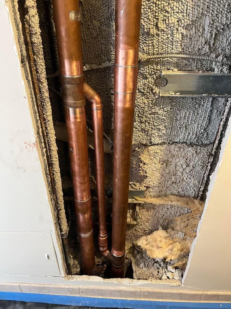 Copper pipes in a wall cavity beside damaged insulation and exposed framing.