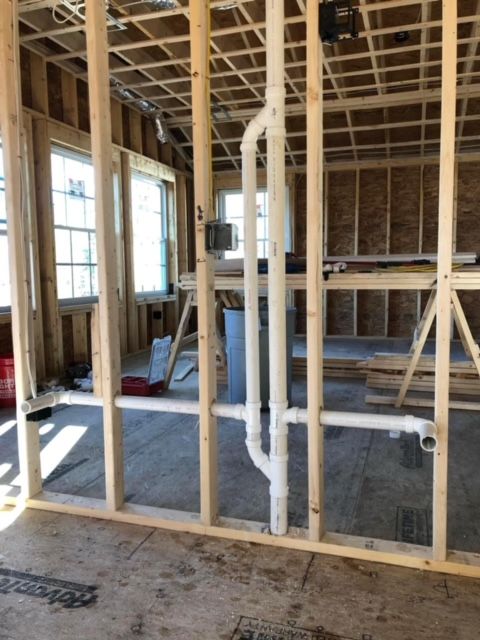 Unfinished house interior with exposed wood framing, white plumbing pipes, and a concrete floor