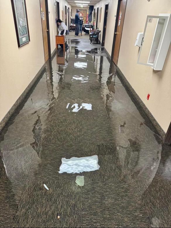 Water-covered hallway with standing floodwater reflecting ceiling lights and a towel on the floor.