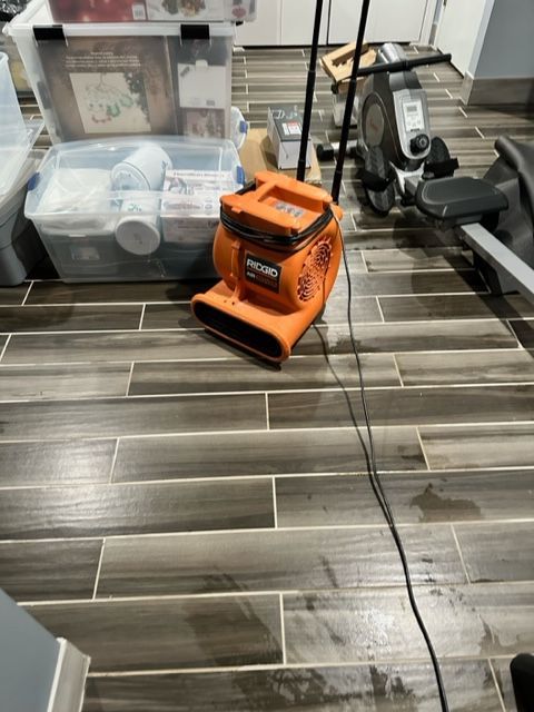 Orange shop vacuum on tiled floor beside a clear bin and a dark exercise machine
