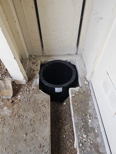 Open floor drain hole beside a wall in a dusty doorway area