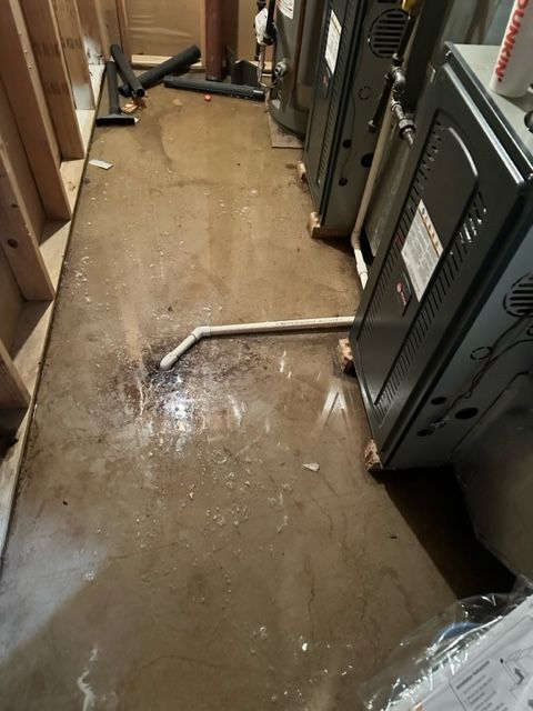 Damaged hallway floor with water spill and a bent metal pipe beside cabinets and machinery