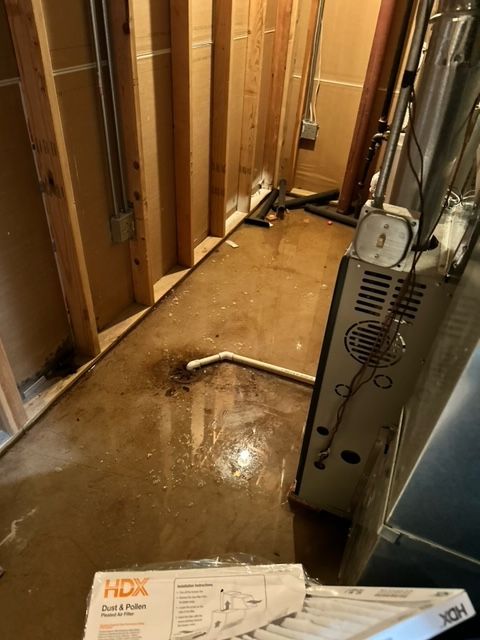 Water-damaged basement hallway with exposed studs, flooded floor, and HVAC unit