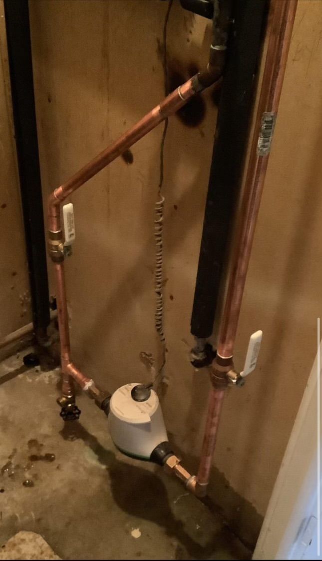 Copper pipes and a white pump or valve assembly in a basement utility area