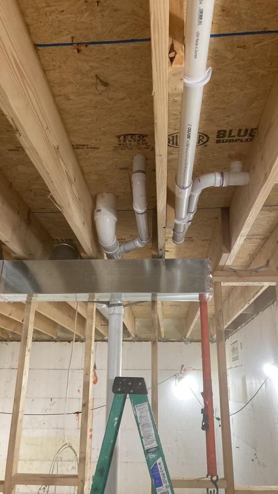 Ceiling framing with exposed plumbing pipes in a room under construction, with a ladder below.