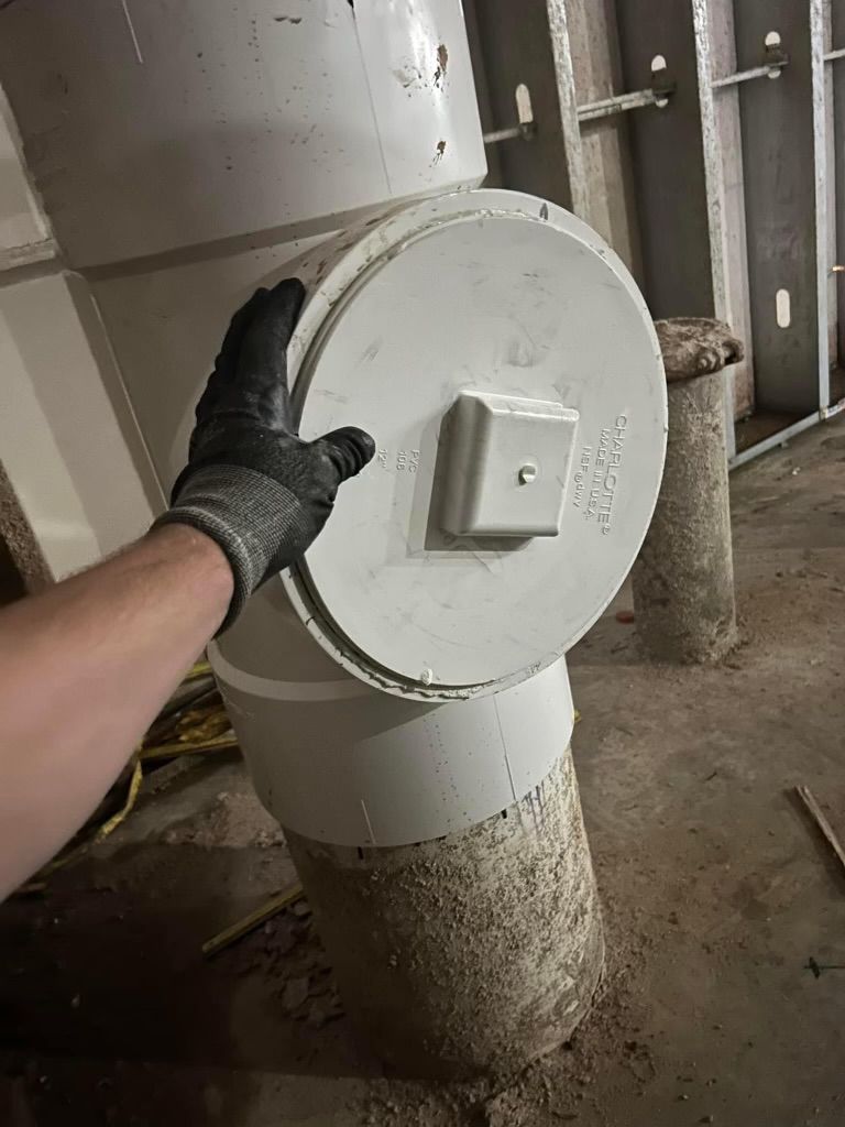Gloved hand holding a round white duct access panel in a dusty industrial room