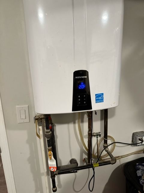 White wall-mounted water heater with a black control panel and visible plumbing in a utility area