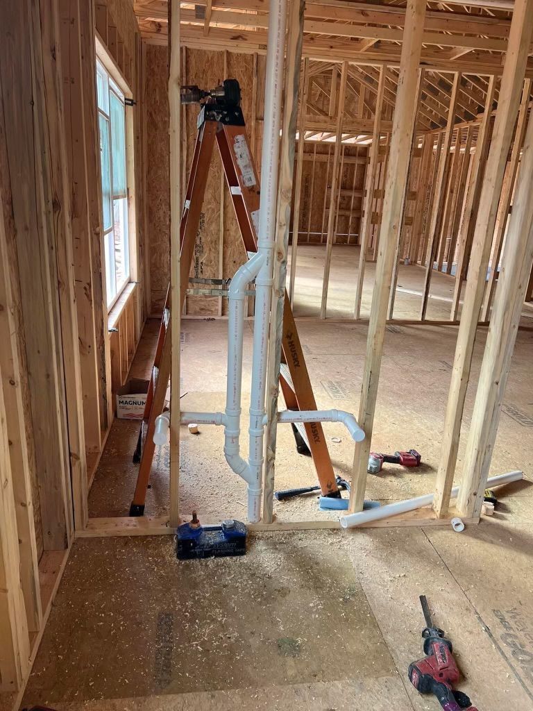 Framed house interior with exposed studs, a ladder, and tools on a rough floor.