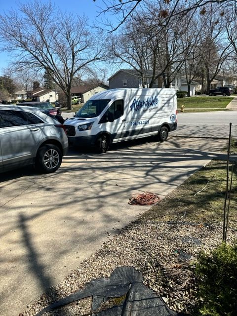 White service van parked behind a gray SUV on a suburban street under leafless trees.