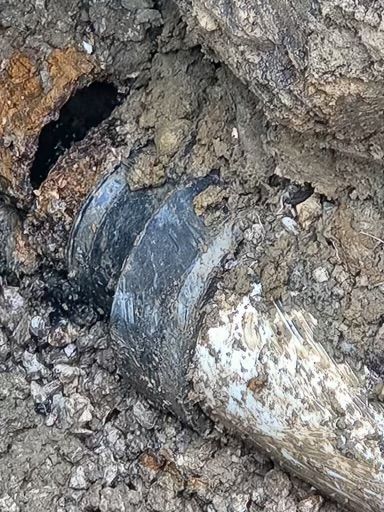 Exposed broken pipe or conduit emerging from muddy soil and debris, with damaged ground around it