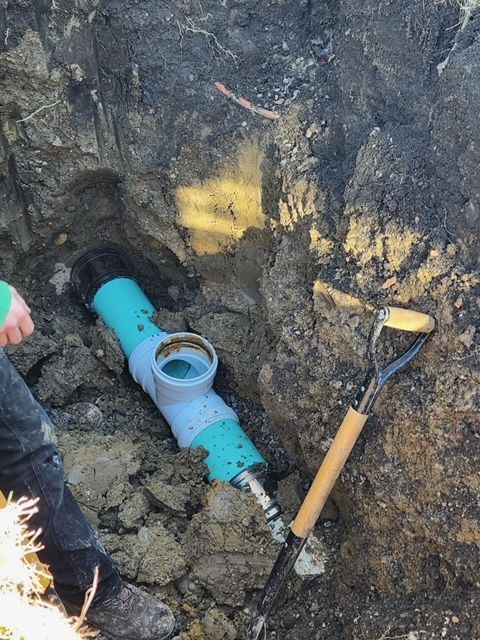 Excavation trench with blue pipe fitting and shovel in muddy soil