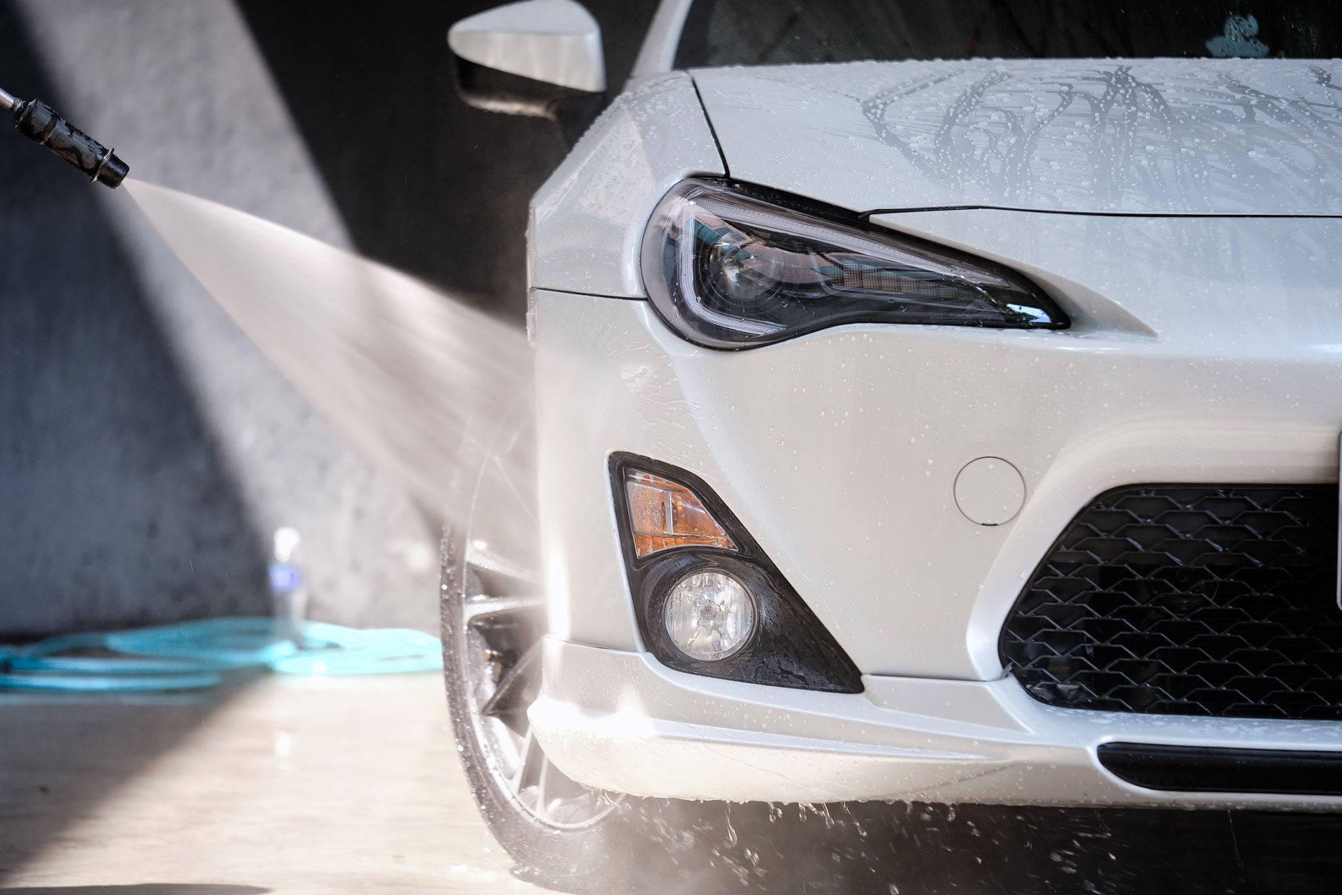White car being washed with a pressure washer; soap and water spraying on the front.