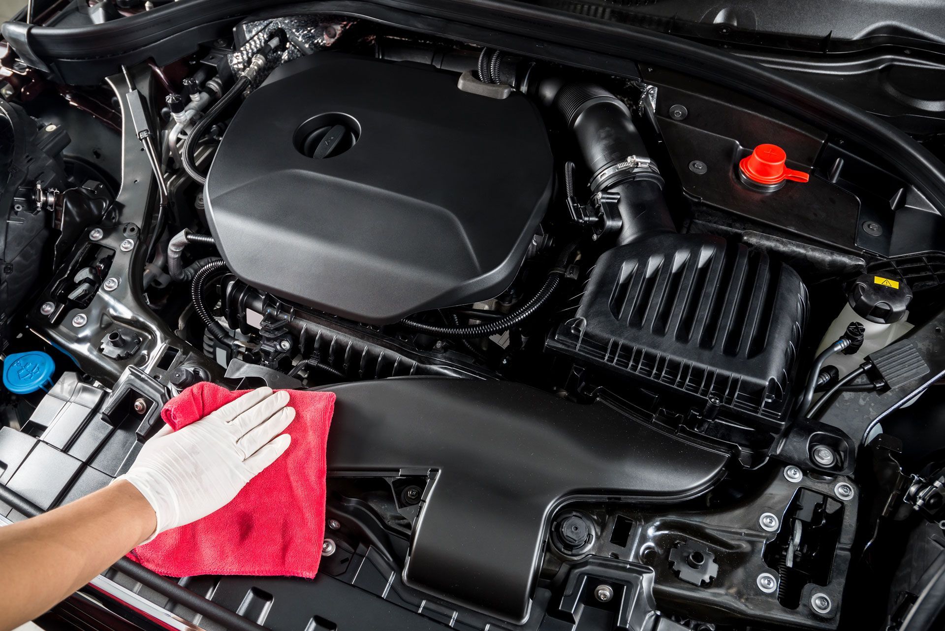 Hand in a glove wiping a red cloth over a clean car engine, in a workshop.