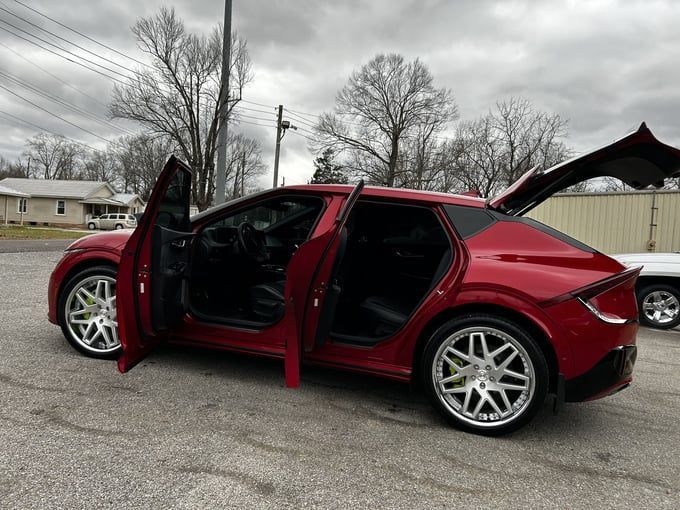 Red Kia EV6 with custom wheels, doors open, on a gray surface with trees and a building in the background.
