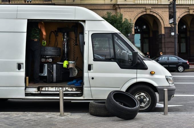 White van with open side door; a person is working on tires. Two tires on the ground.