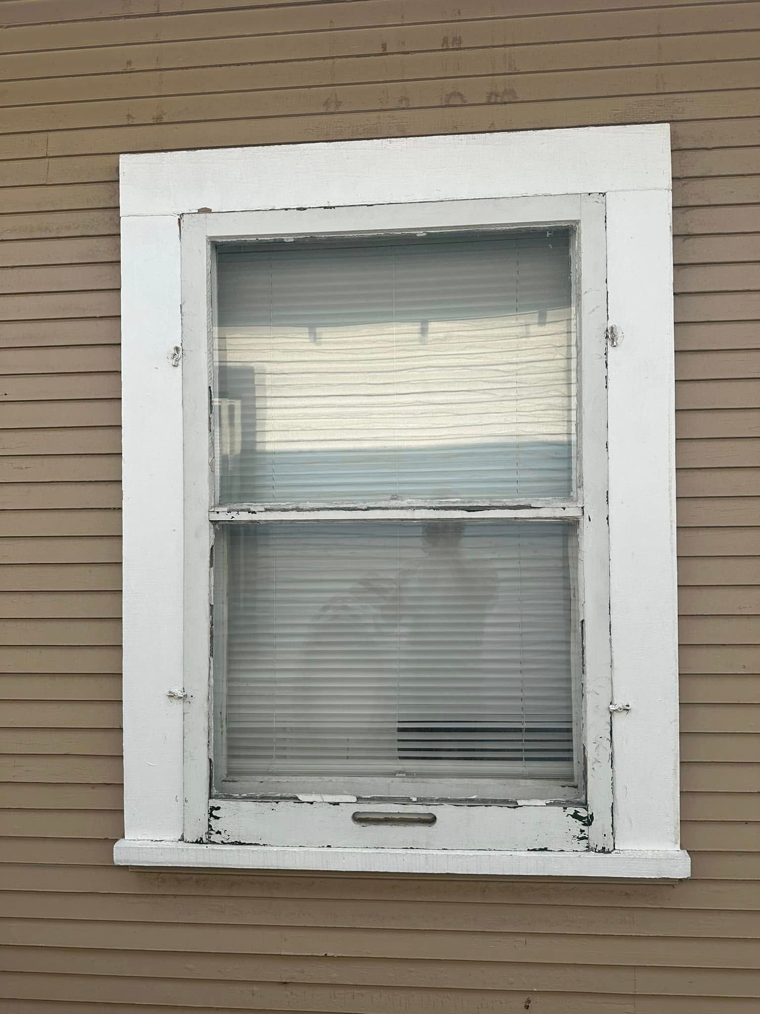 A window with blinds on it is on the side of a house.