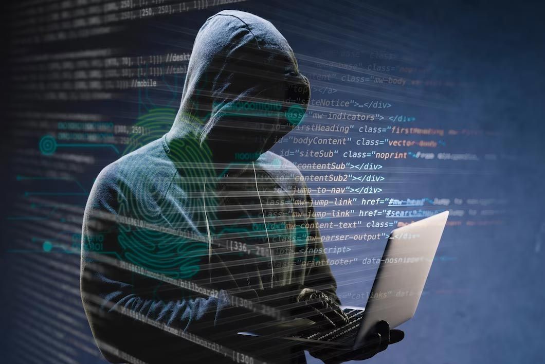 Hooded figure using a laptop with code glowing in the background, evoking a cyberattack scene
