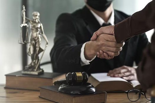 Handshake over a legal desk with a gavel, scales of justice, and a masked attorney in the background