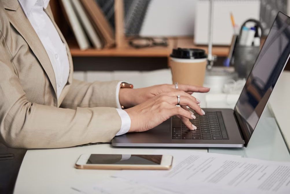 Person typing on a laptop at a desk with a phone and coffee cup nearby