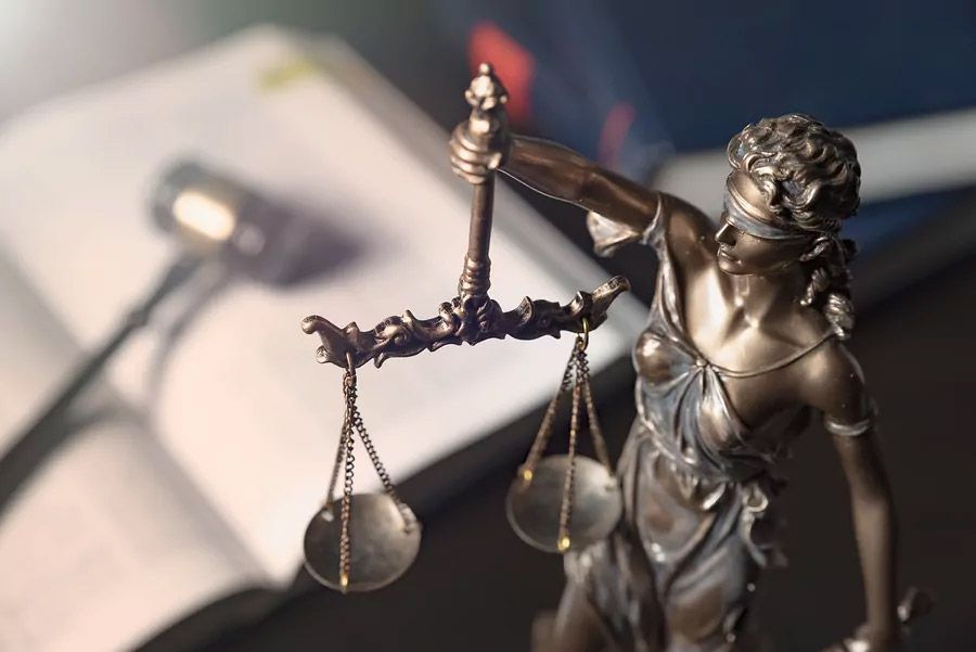 Bronze Lady Justice statue holding scales, with blurred gavel and papers in the background