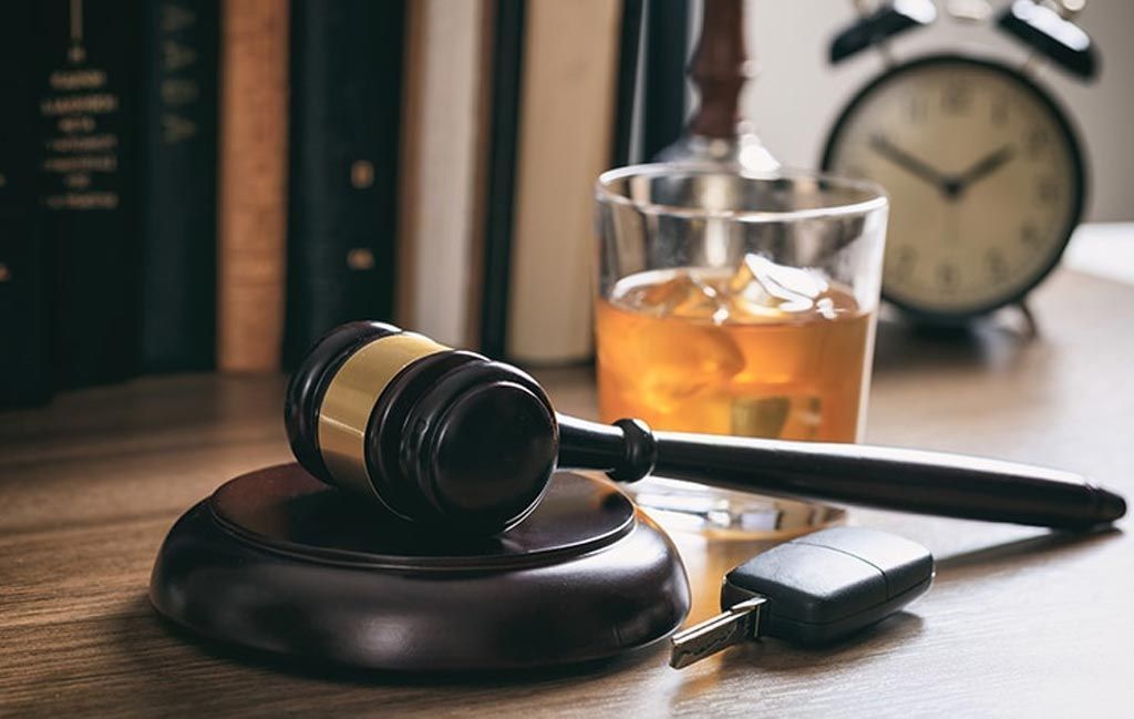 Judge’s gavel on a desk beside a key, glass of whiskey, and clock in a courtroom setting