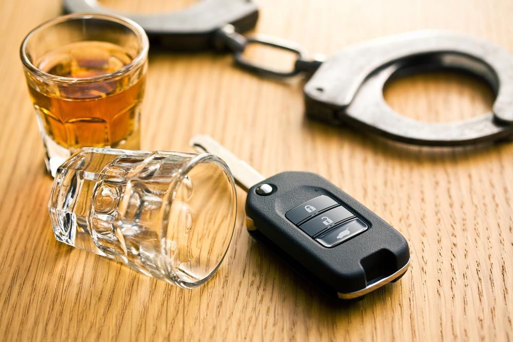 Handcuffs, overturned whiskey glass, and car key on a wooden table, suggesting drunk driving arrest