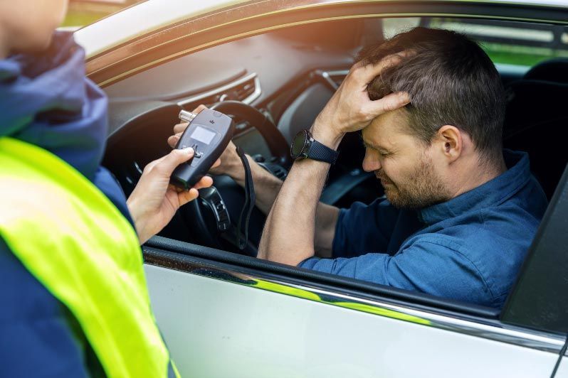 Driver in blue shirt stopped by officer holding a breathalyzer through the car window