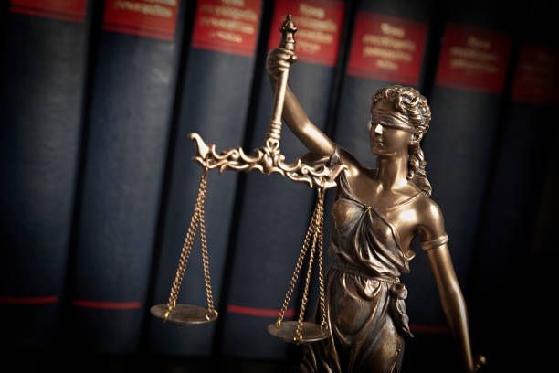 Bronze Lady Justice statue holding scales before blurred law books